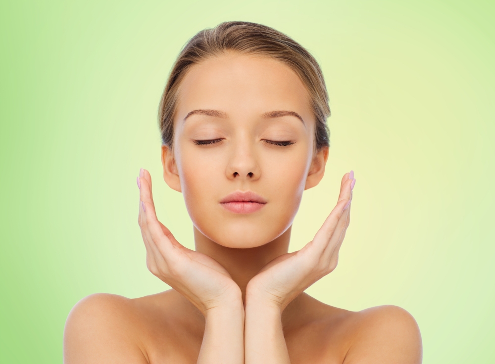 beauty, people, skincare and health concept - young woman face and hands over green background
