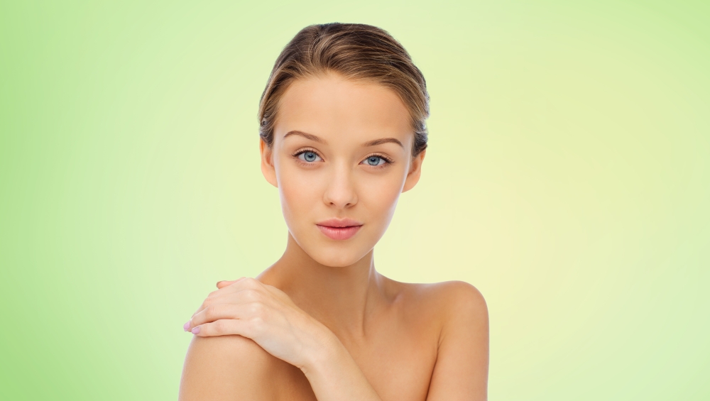 beauty, people, body care and health concept - smiling young woman face and hand on bare shoulder over green background