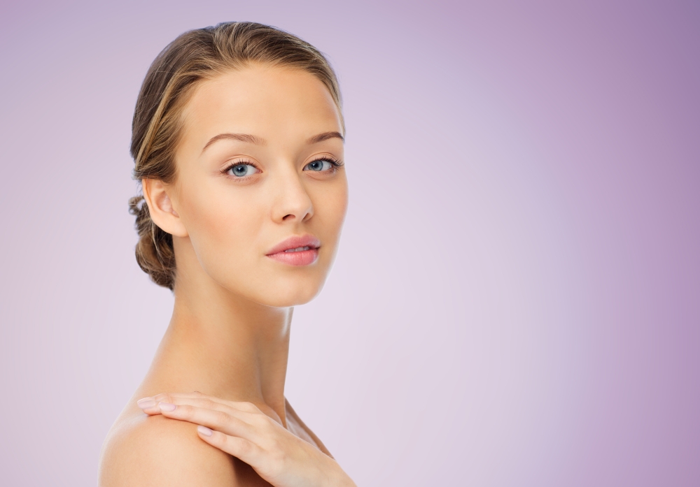 beauty, people, body care and health concept - smiling young woman face and hand on bare shoulder over violet background
