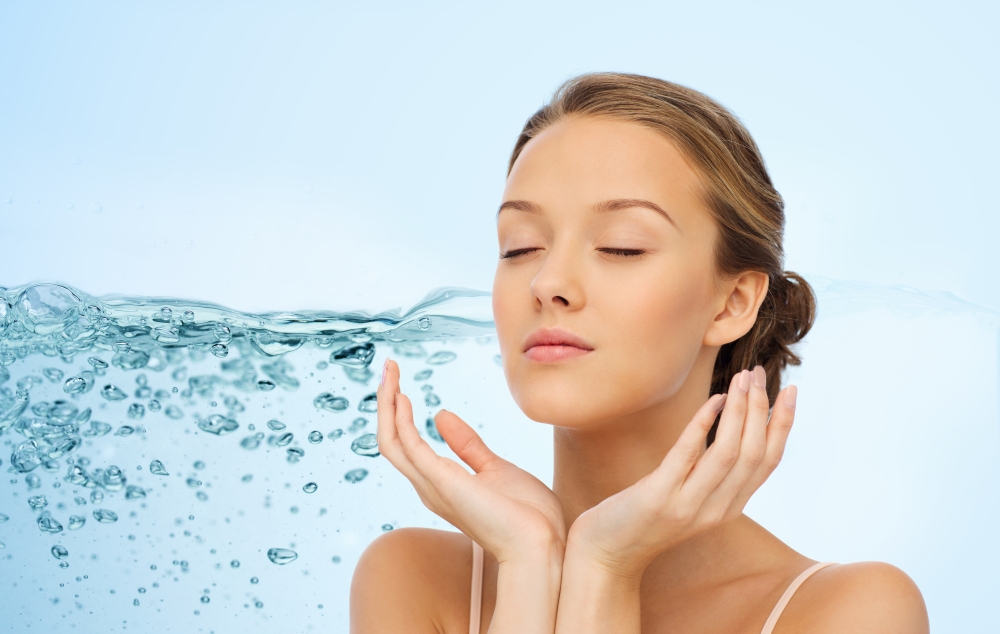 beauty, people, moisturizing, skin care and health concept - young woman face and hands over water splash background