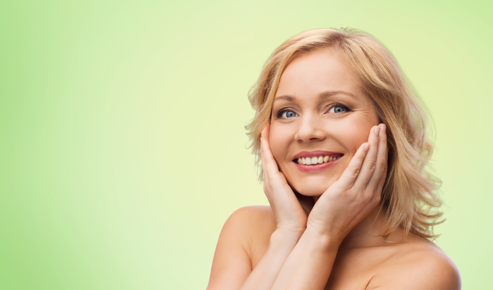 beauty, people and skincare concept - smiling woman with bare shoulders touching face over green natural background