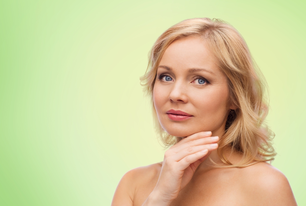 beauty, people and skincare concept - smiling woman with bare shoulders touching face over green natural background