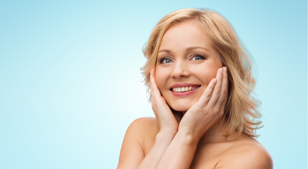 beauty, people and skincare concept - smiling woman with bare shoulders touching face over blue background