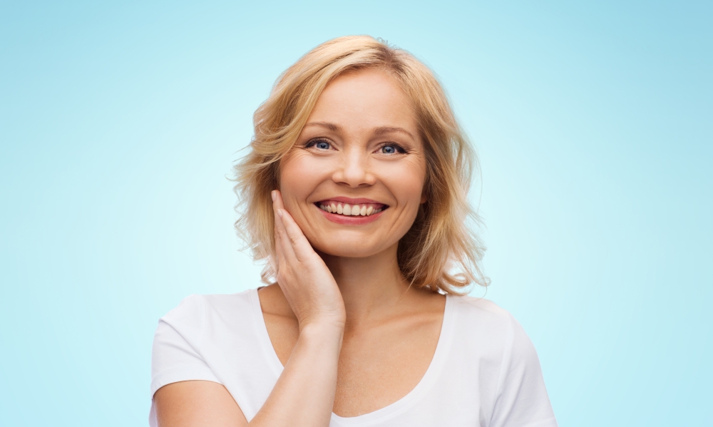 beauty, people and skincare concept - smiling woman in white shirt touching face over blue background