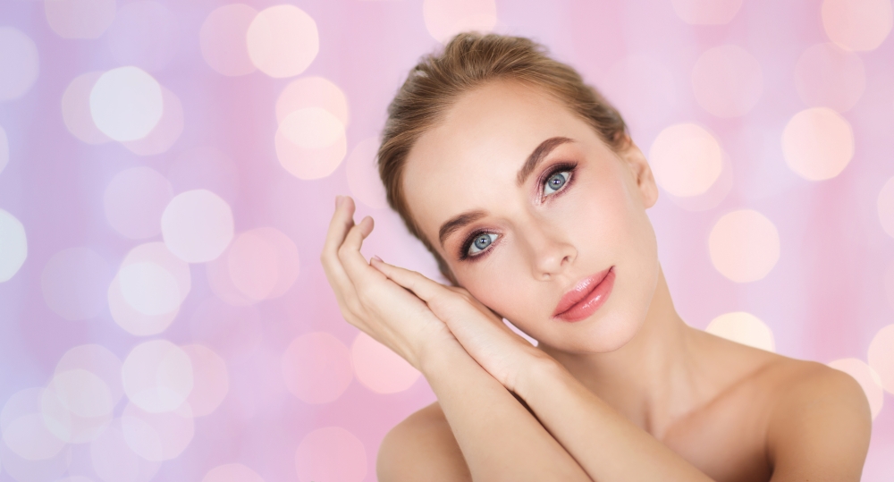 beauty, people and bodycare concept -beautiful young woman face and hands over rose quartz and serenity lights background
