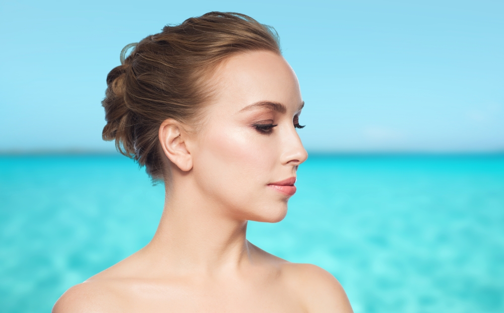 health, people, plastic surgery and beauty concept - beautiful young woman face over blue sea and sky background