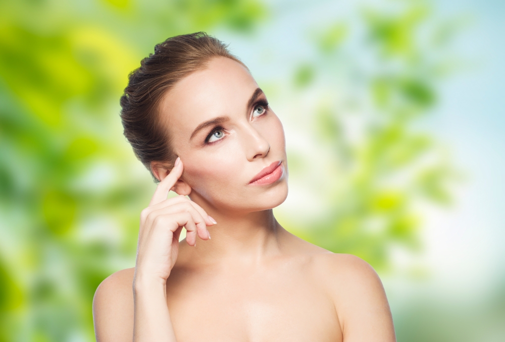 beauty, people, eco and health concept - beautiful young woman touching her face over green natural background