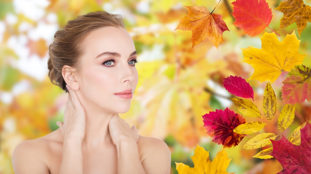 beauty, people, season and bodycare concept -beautiful young woman face and hands over autumn leaves background