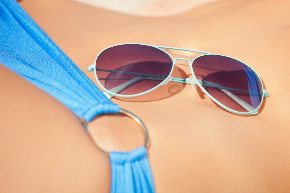 closeup picture of female belly, bikini and shades.