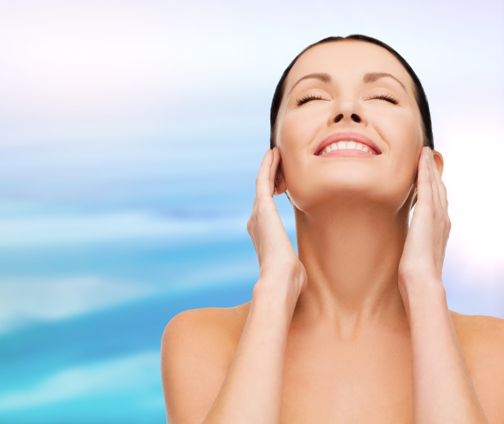health, spa and beauty concept - clean face and hands of beautiful smiling woman with closed eyes