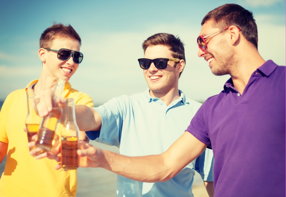 summer, holidays, vacation and happy people concept - group of friends having fun on the beach with bottles of beer or non-alcoholic drinks