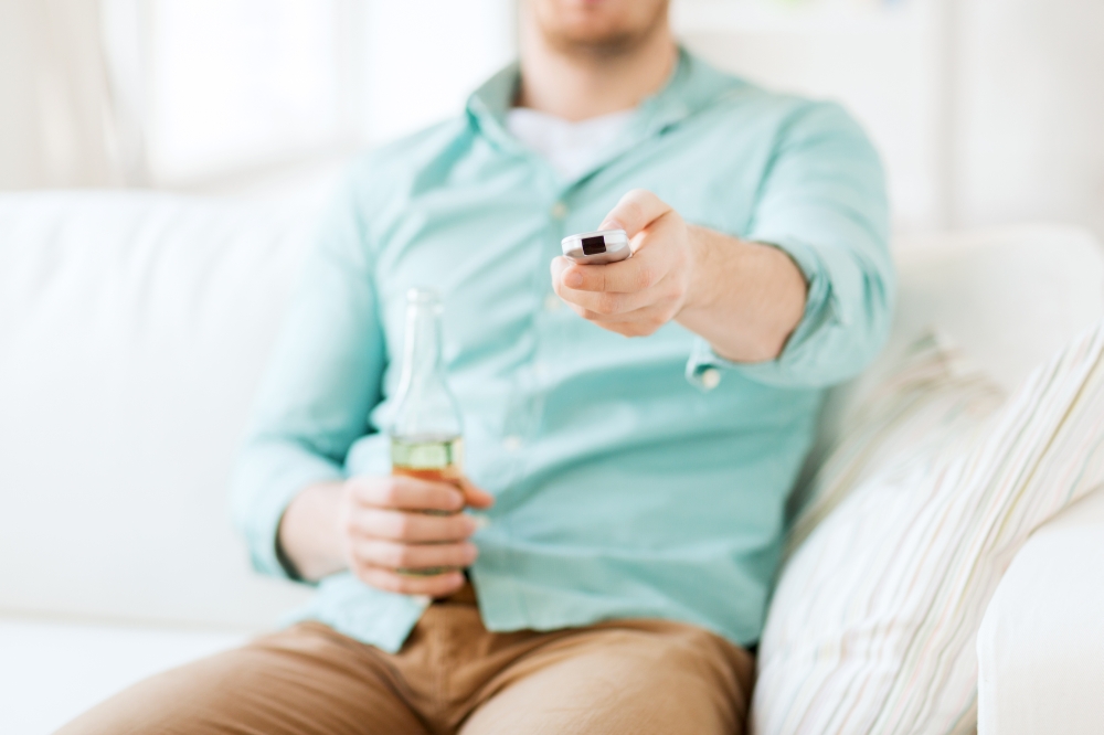 drinks, television, leisure and people concept - man changing tv channels and drinking beer at home