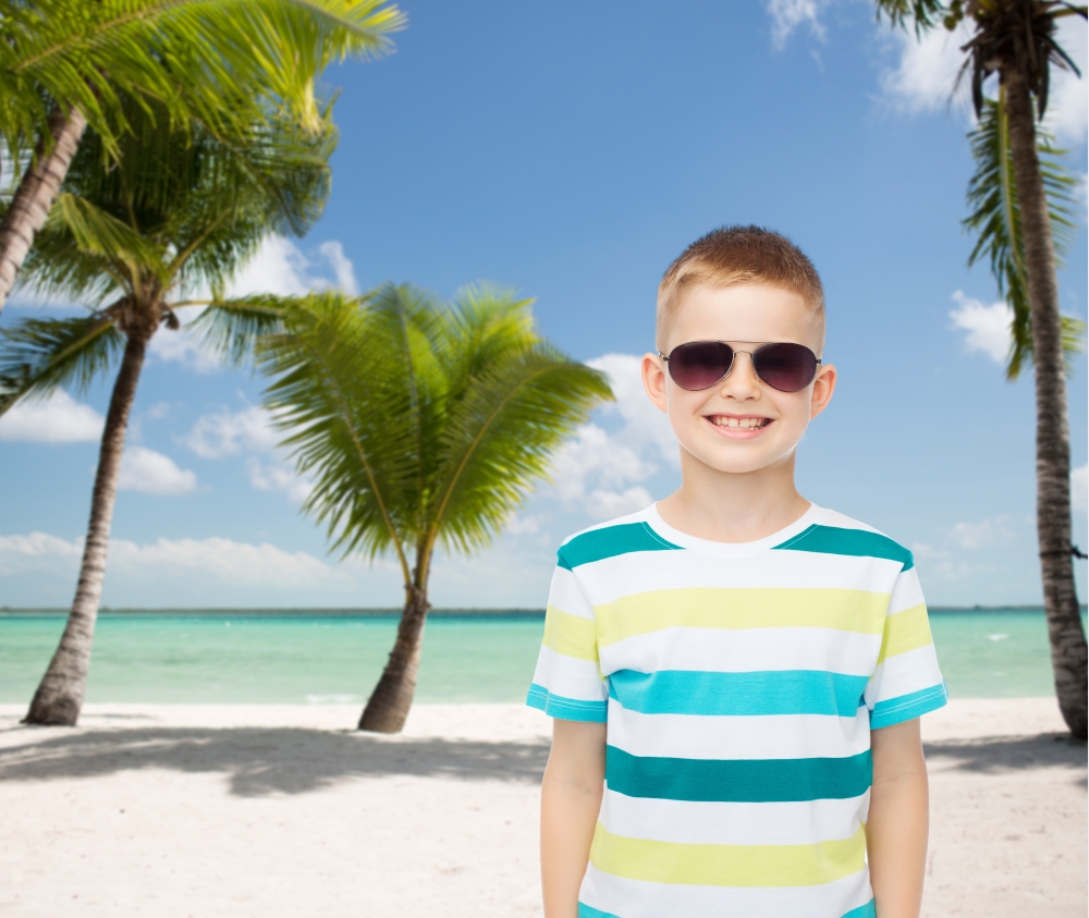 childhood, summer, travel, vacation and people concept - smiling little boy wearing sunglasses over beach background