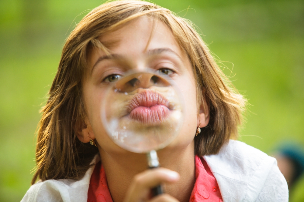 Close-up portrait of a girl that plays with magnifying glass. Funny lips