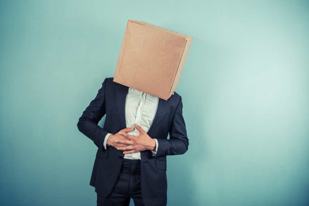 A businessman with a cardboard box on his head is having stomach pains