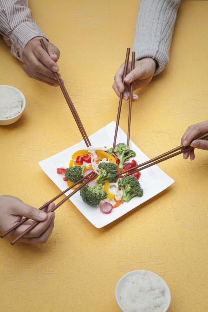 Close up of people holding chopsticks and sharing one dish
