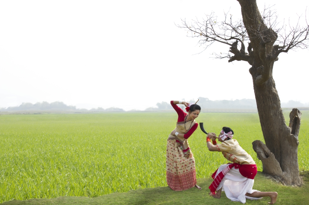 Bihu man blowing on a pepa while Bihu woman dances to his tune