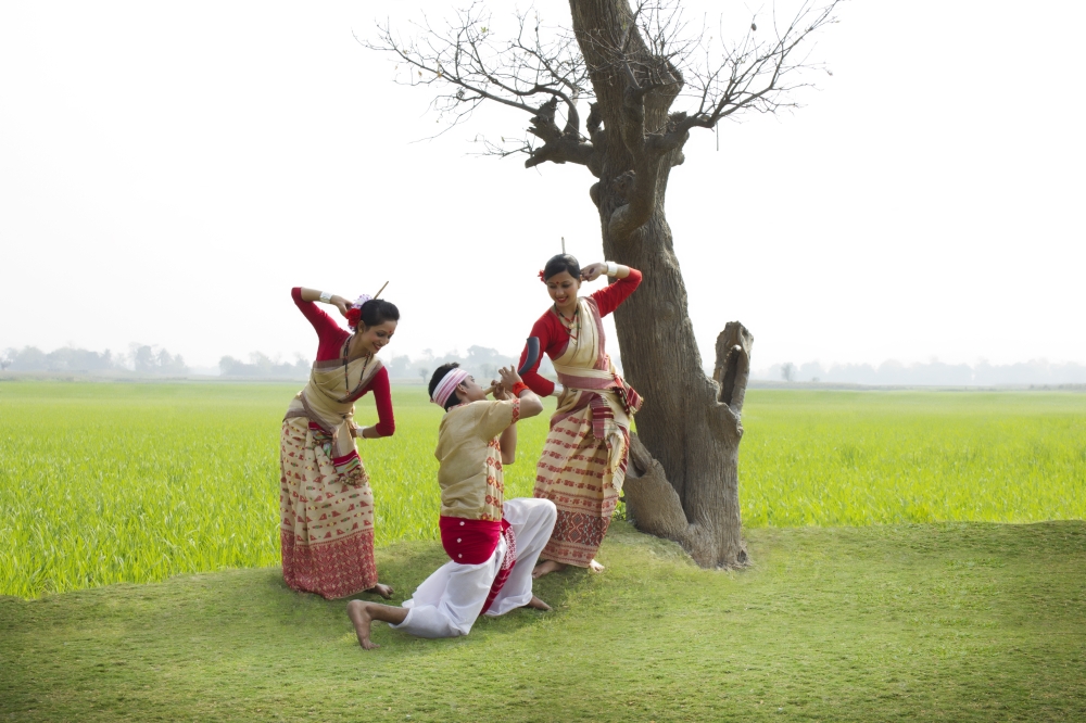 Bihu man playing on a pepa while Bihu women dance to his tune