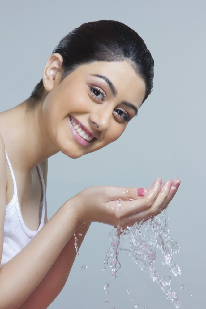 Portrait of happy woman washing face with water against blue background