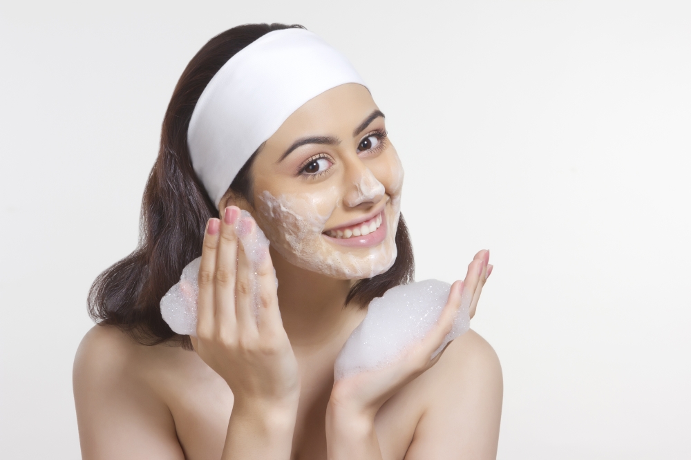 Portrait of happy woman applying soap sud on face against white background