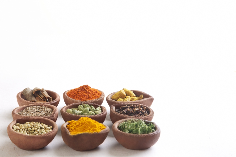 Variety of Indian spices in oil lamps over white background