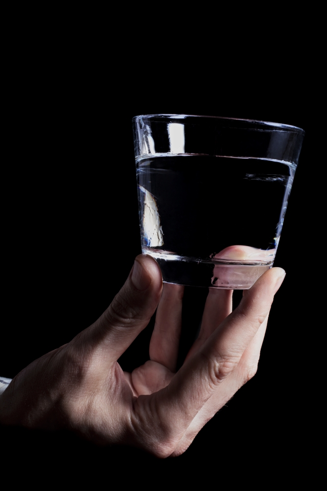 Man&rsquo;s hand holding a clear glass of water on a black background