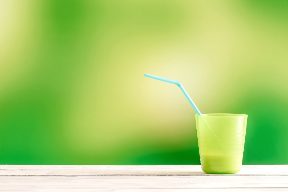 Green cup with a blue straw on a wooden table