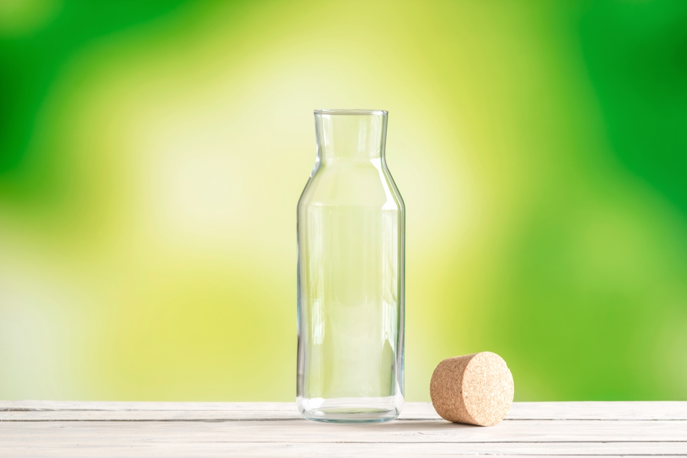Empty glass bottle with a cork on green background