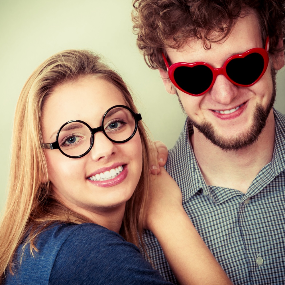Happy young man in heart shaped glasses and woman. Smiling friends couple in studio.. Happy couple man and woman in glasses.