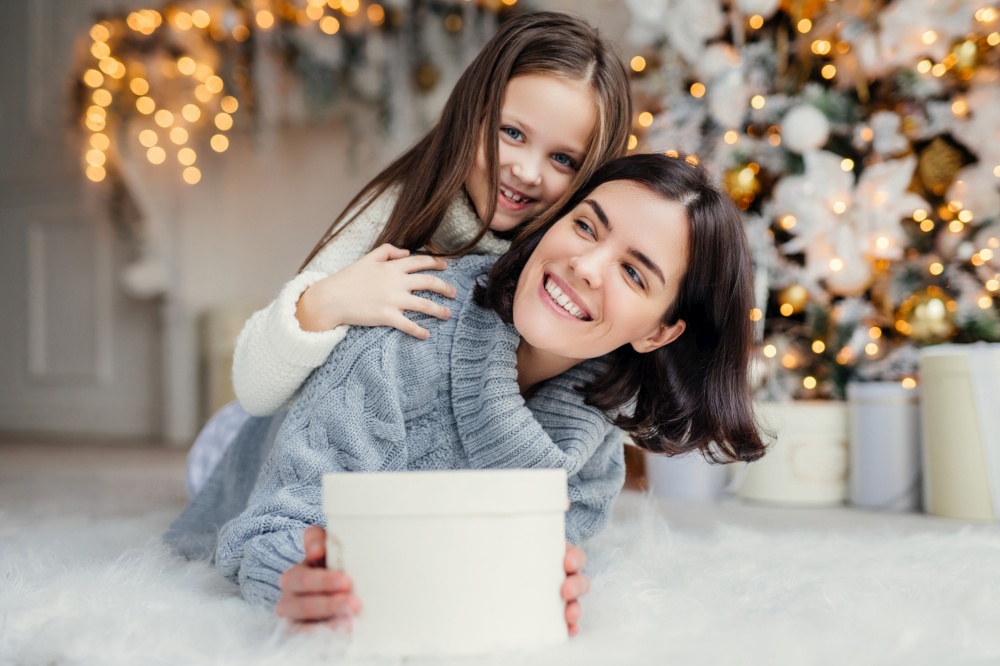 Cheerful mother and child with a present, sharing a joyous moment in front of a glowing Christmas tree