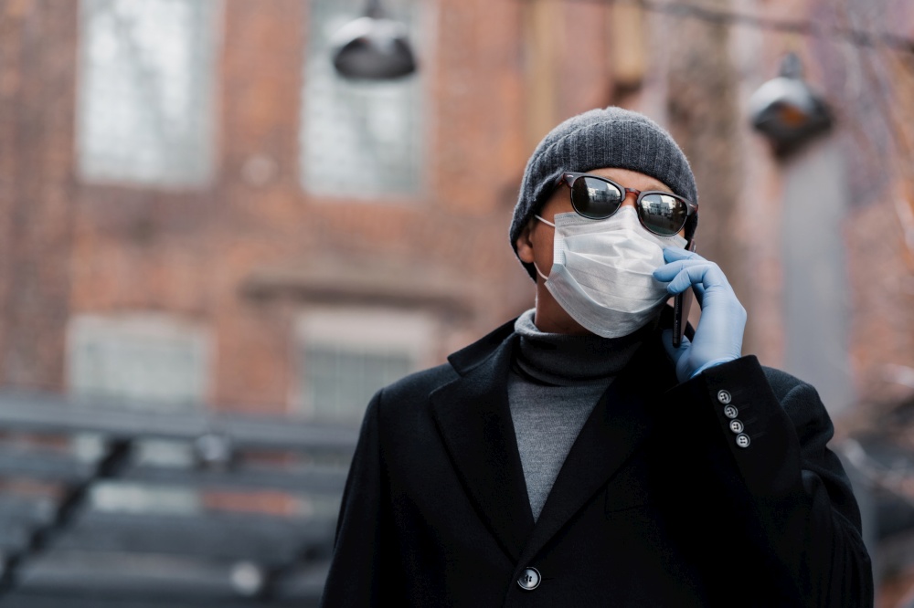 Man in winter clothes speaking on a mobile phone, wearing a surgical mask and gloves