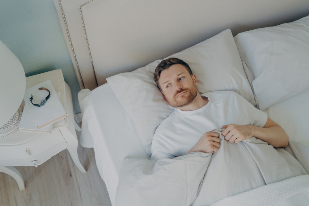 Man lying in bed unable to sleep, looking stressed and contemplative, insomnia concept.