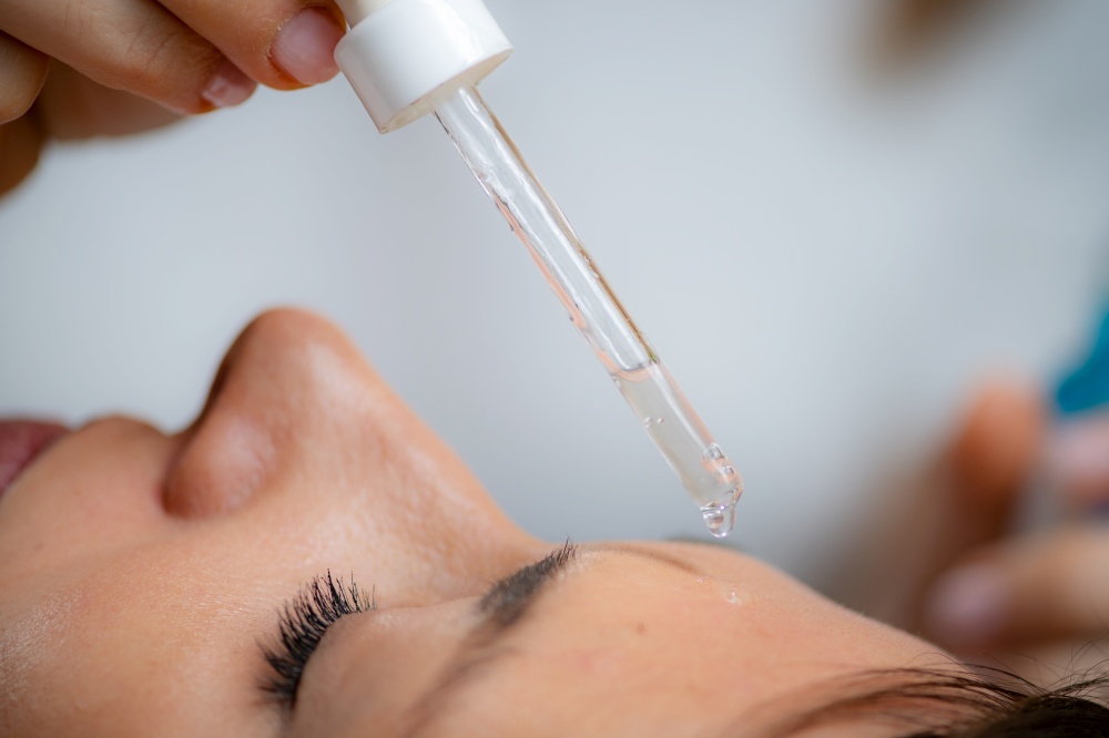 Professional cosmetician applying hyaluronic acid serum for a radiant, hydrated complexion. Professional cosmetician applying hyaluronic acid serum on womans face for a radiant, hydrated complexion
