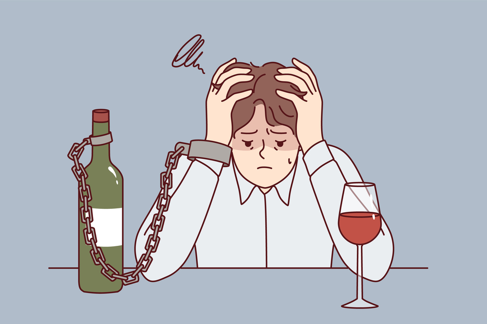 Man suffering from alcohol addiction is chained to bottle of wine, sitting at table clutching head. Guy with liquor addiction fell into depression after being betrayed by girlfriend. Man suffering from alcohol addiction is chained to bottle of wine, sitting at table clutching head