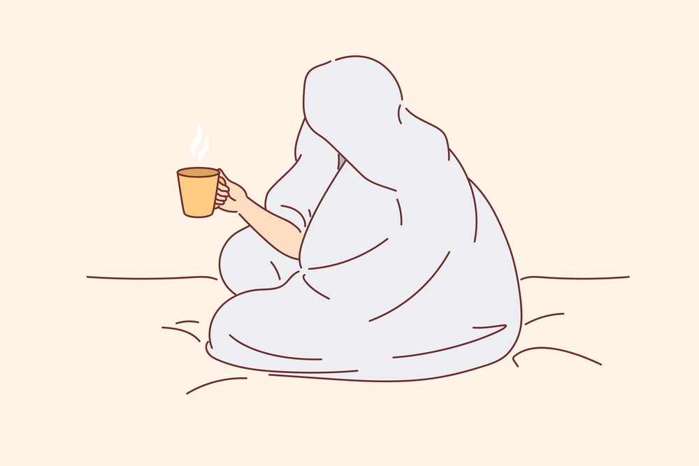 Man drinks coffee sitting on bed and wrapped in blanket to warm up after walk along winter street. Cup of hot coffee in hands of human enjoying comfort and energizing thanks to drink.. Man drinks coffee sitting on bed and wrapped in blanket to warm up after walk along winter street