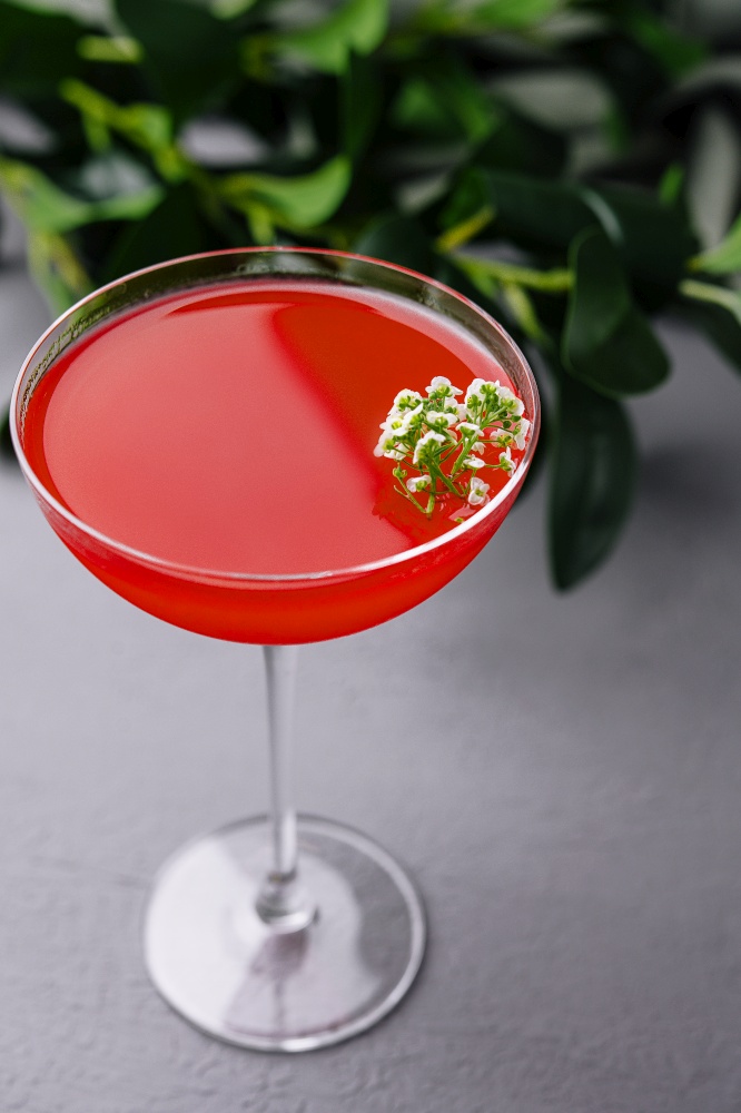 Vibrant red cocktail in a stemmed glass, adorned with white flowers, presented on a sleek surface. Elegant red cocktail with floral garnish