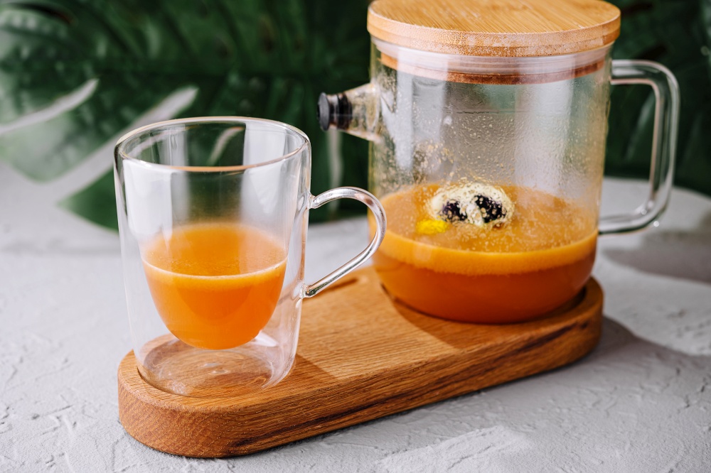 Vibrant orange fruit smoothie freshly blended, pouring into a clear glass on a wooden stand. Freshly blended fruit smoothie pouring into glass