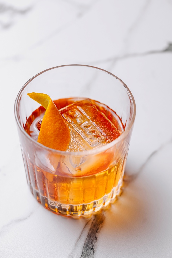 Close-up of a classic old fashioned cocktail garnished with a fresh orange twist on a marble surface. Elegant old fashioned cocktail with orange twist