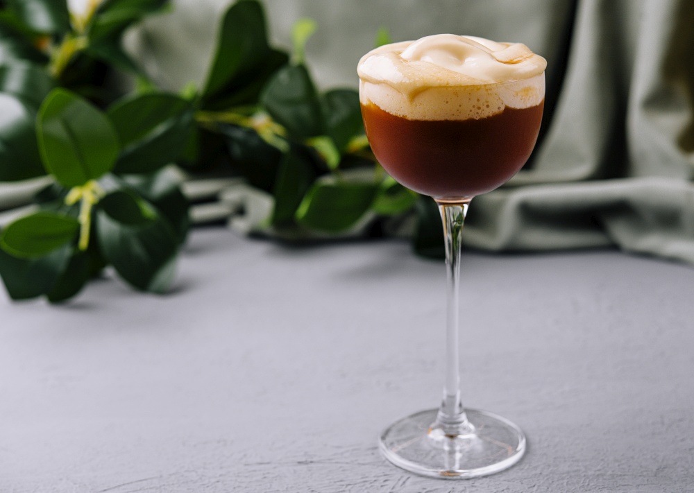 Espresso martini with a creamy foam topping, presented in a stemmed glass against a neutral background. Elegant espresso martini cocktail on table