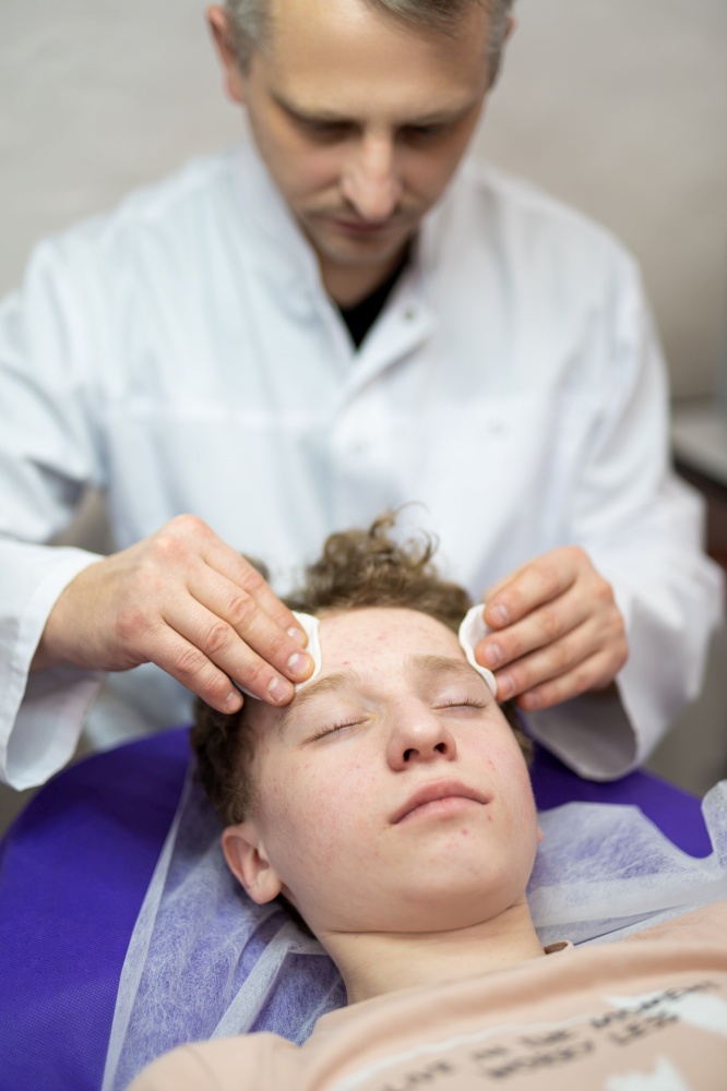a cosmetologist doctor makes cosmetic procedures on the face of a young guy in a beauty salon