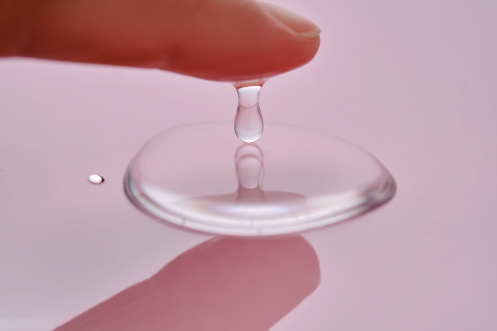 A finger touches a drop of cosmetic product on a pink background. High quality photo.. A finger touches a drop of cosmetic product on a pink background.