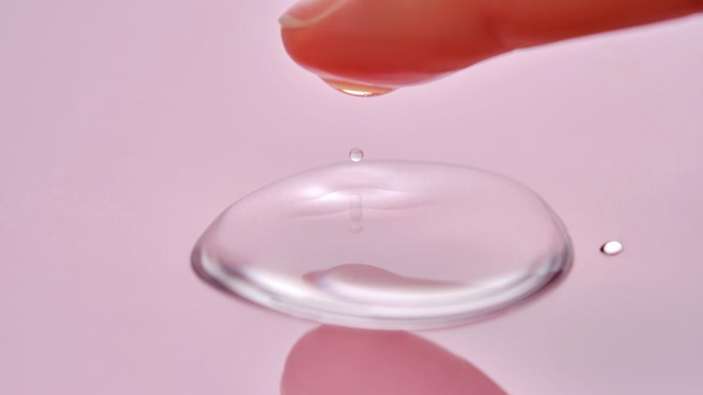 A finger touches a drop of cosmetic product on a pink background. High quality photo.. A finger touches a drop of cosmetic product on a pink background.