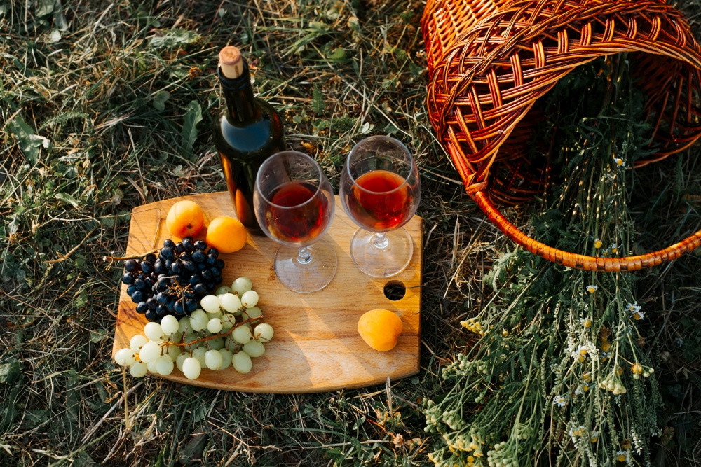 Top view bottle of red wine, two glasses, fruits, grapes, peaches, wicker basket with wildflowers at sunset outdoors. Romantic date picnic outdoors, still life.. Top view bottle of red wine, two glasses, fruits, grapes, peaches, wicker basket with wildflowers at sunset outdoors. Romantic date picnic outdoors, still life