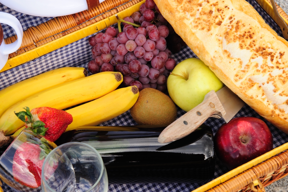 Closeup of the contents of a picnic backet these include red wine, grapes, red and green apples, kiwi fruit, bannas, strawberries amd a loaf of french bread. Inside A Picnic Basket