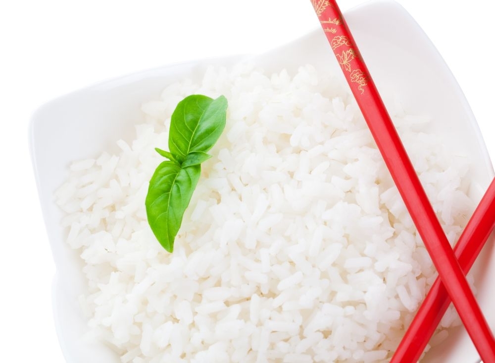 A macro shot of red chopsticks and white rice delicately garnished with a sprig of basil.  Isolated with clipping path.