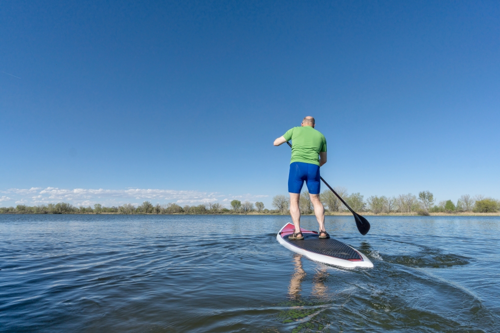senior male on SUP (stand up paddleboard) on a lake under Colorado blue sky
